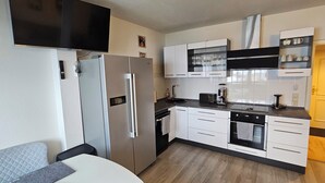 Eine kompakte Küche mit Kühlschrank, Backofen und Mikrowelle. Es gibt Schränke und eine Arbeitsplatte mit einer Kaffeemaschine.