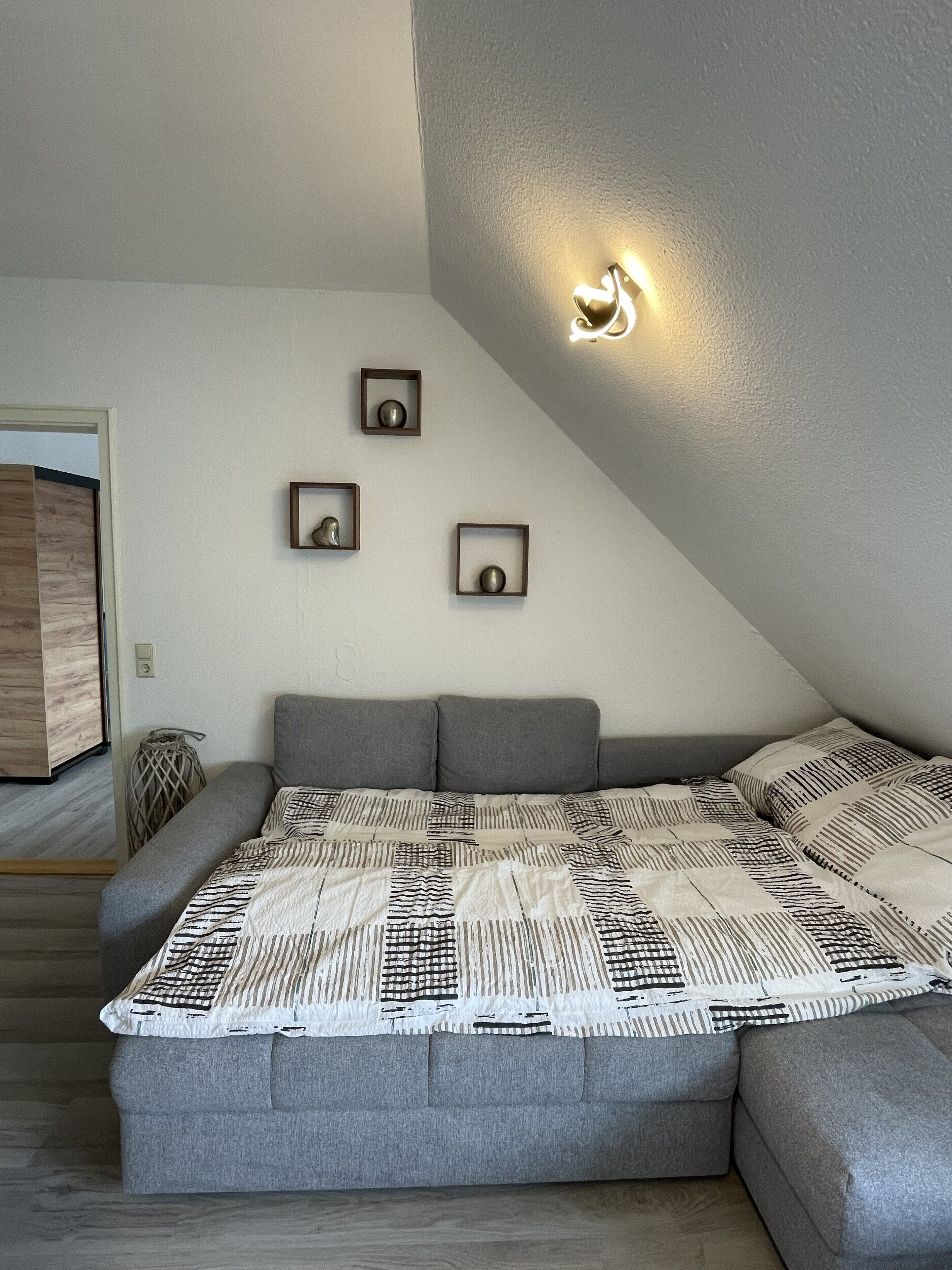 A modern bedroom with a gray sectional sofa, a patterned quilt, and three wall-mounted picture frames.
