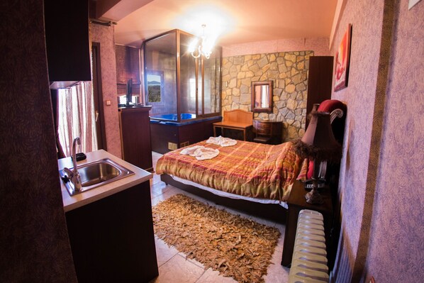 A bedroom with a bed, a wooden nightstand, a dresser, a mirror, and a stone wall.