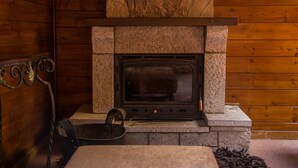 Una chimenea de piedra con una rejilla metálica, un cubo de metal y un espacio para almacenar leña.