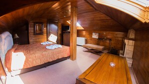 Un dormitorio acogedor en el ático con techo de madera, una cama, una mesa y una pequeña zona de kitchenette.