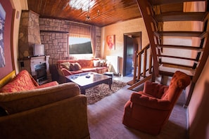 A cozy living room with a stone fireplace, a sofa, a red armchair, and a staircase leading to an upper level.