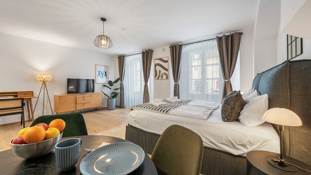 Ein modernes Hotelzimmer mit einem Bett, Nachttisch, Lampe und einem Essbereich mit Tisch, Stühlen und einer Obstschale.