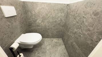 A small, modern bathroom with a toilet, a roll of toilet paper, and a black toilet brush.