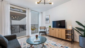 Ein modernes Wohnzimmer mit Sofa, Couchtisch, Fernseher und einem großen Fenster mit Balkon.