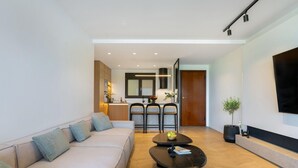 Ein modernes Wohnzimmer mit einer Couch, einem Couchtisch, einem Essbereich mit Stühlen, einer Küche im Hintergrund und einem an der Wand befestigten Fernseher.