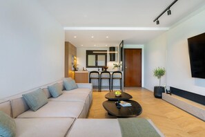 Un salon moderne avec un canapé, une table basse, un coin repas avec des chaises, une cuisine en arrière-plan et un téléviseur fixé au mur.