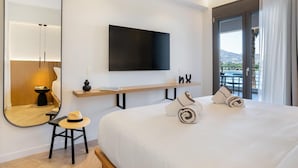 Ein Hotelzimmer mit einem großen Bett, einem Wand-Fernseher, einem Holzregal, einem Spiegel und Blick ins Freie.