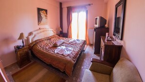 A hotel room with a bed, a desk with a television, a chair, a lamp, and a painting on the wall. - Budget Double or Twin Room (Kryonérion, limni plastira, karditsa)