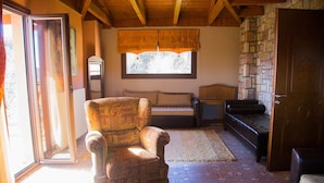 A room with a patterned armchair, a sofa, a small table, and a stone wall. - Budget Double or Twin Room (Kryonérion, limni plastira, karditsa)