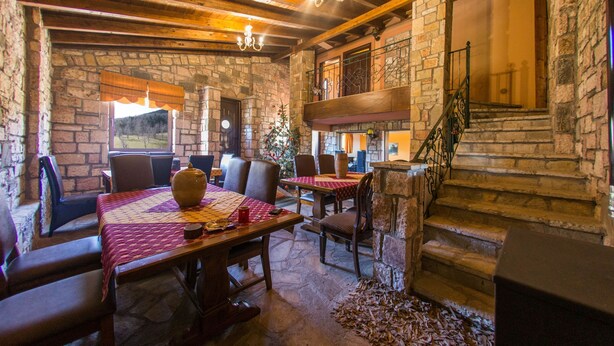 A rustic dining area with stone walls, wooden beams, and a chandelier. Tables are set with red tablecloths and chairs. - Budget Double or Twin Room (Kryonérion, limni plastira, karditsa)