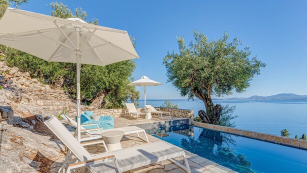 Un espace aménagé au bord de la piscine, avec des chaises longues et des parasols, offrant une vue sur un plan d’eau et des montagnes.