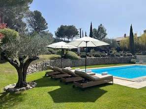 Una piscina con sillones de descanso y sombrillas, rodeada por un césped bien cuidado y un muro de piedra.