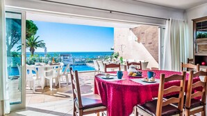 Een eethoek met een tafel gedekt voor twee personen, met uitzicht op een zwembad en de zee.