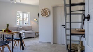 Een moderne woonkamer met een bank, eettafel en stoelen. Er is een trap met een houten afwerking en een decoratief wandobject.