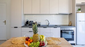 Een moderne keuken met witte kasten, een roestvrijstalen koelkast en een houten eettafel met een fruitmand als decoratie.