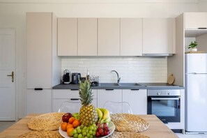 A modern kitchen with white cabinets, a stainless steel refrigerator, and a dining table set with fruits and woven placemats. - Terra Nuova Zante in Zakynthos (Zakynthos)