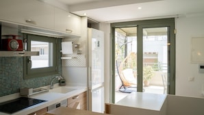 A modern kitchen with a built-in stove, a refrigerator, and a window overlooking a balcony. - Eclectic Urban Nest in Heraklion (Heraklion)