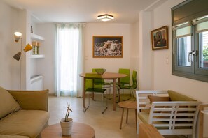 Una sala de estar moderna con un sofá, una mesa de comedor con sillas, una mesita con una planta y una ventana con persianas.