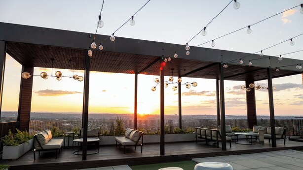 Un patio al aire libre con asientos e iluminación de guirnaldas, con vista a un paisaje urbano al atardecer.