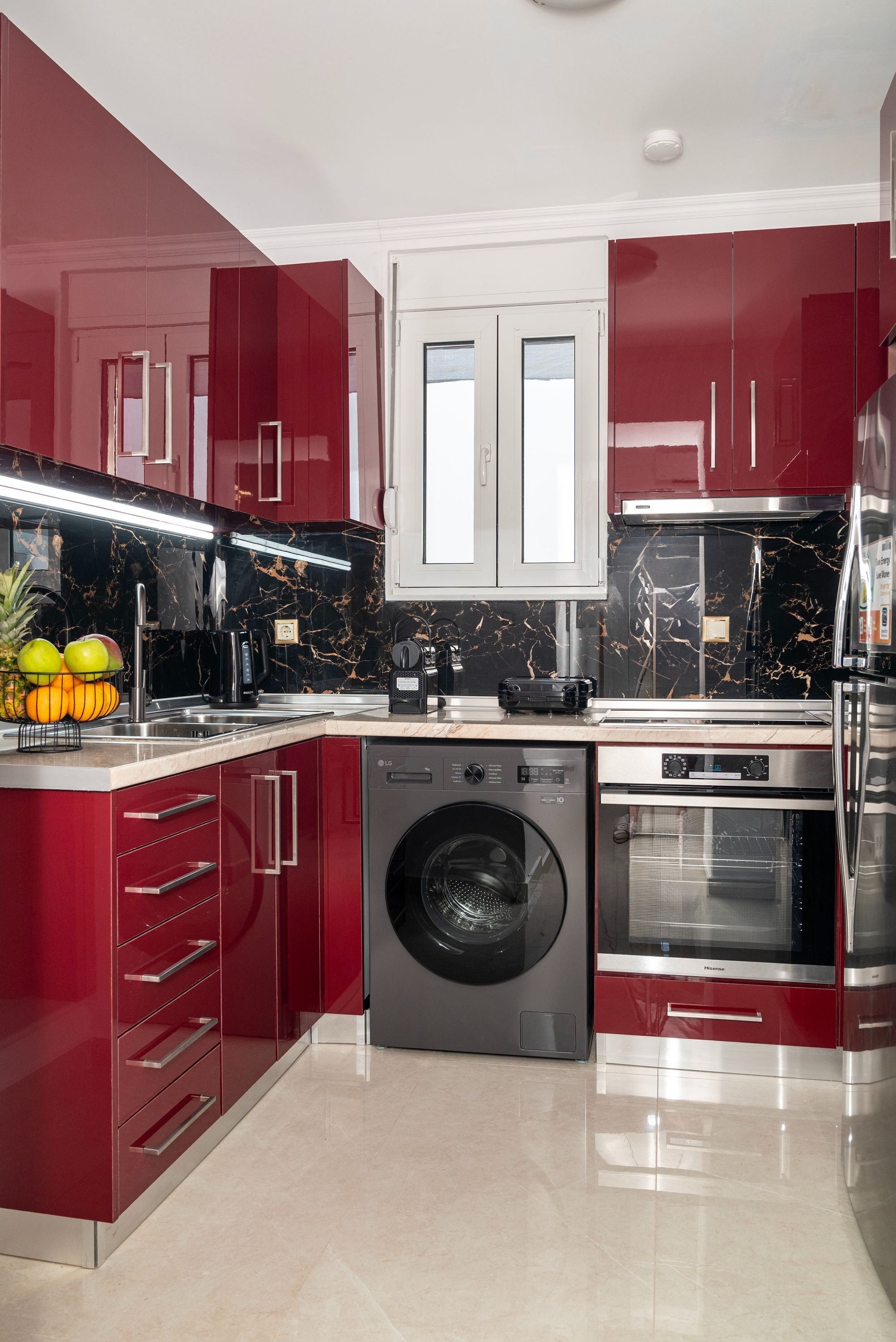 Een moderne keuken met rode kastjes, een wasmachine en een magnetron.