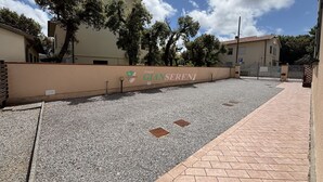 Ein gepflasterter Außenbereich mit Kiesweg, Ziegelpflaster und einer niedrigen Mauer mit einem Logo.