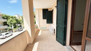 Ein Balkon mit Fliesenboden, einer grünen Tür und einem Fenster mit Rollläden.