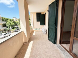 Ein Balkon mit Fliesenboden, einer grünen Tür und einem Fenster mit Rollläden.