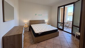 Ein Schlafzimmer mit Bett, Schreibtisch, Stuhl und einer Schiebetür zum Balkon.