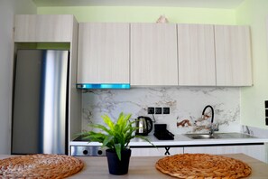 Eine moderne Küche mit hellen Holzschränken, einem Edelstahl-Kühlschrank, einer Marmor-Spritzschutzwand und einem Spülbecken mit Armatur.