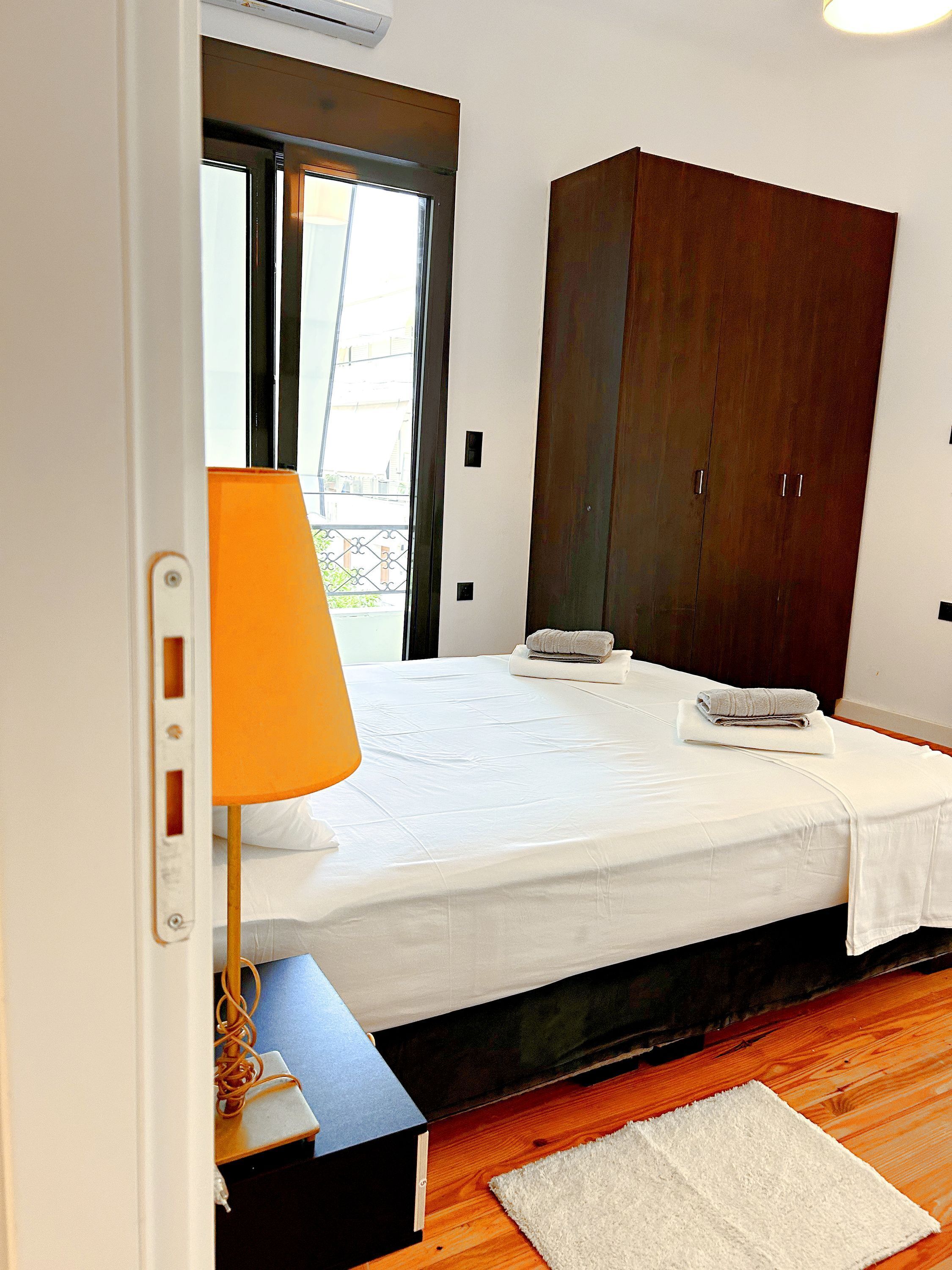 A bedroom with a bed, a wooden wardrobe, a nightstand, and a window with a view.