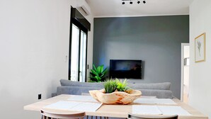 Un espace repas moderne avec une table en bois, deux chaises, un canapé gris et un téléviseur à écran plat fixé au mur.