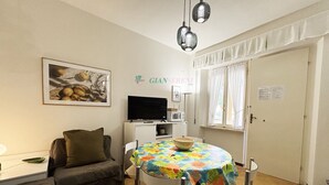A cozy living room with a sofa, a dining table with a colorful tablecloth, a flat-screen TV, and a microwave. - 3 rooms 4 beds Conchiglia area. Il Gabbiano-Rif. Il gabbiano (San Vincenzo)