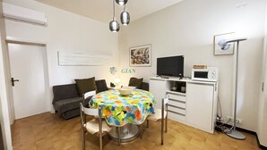 A small, well-lit room with a dining table, chairs, a sofa, a television, a microwave, and a floor lamp. - 3 rooms 4 beds Conchiglia area. Il Gabbiano-Rif. Il gabbiano (San Vincenzo)
