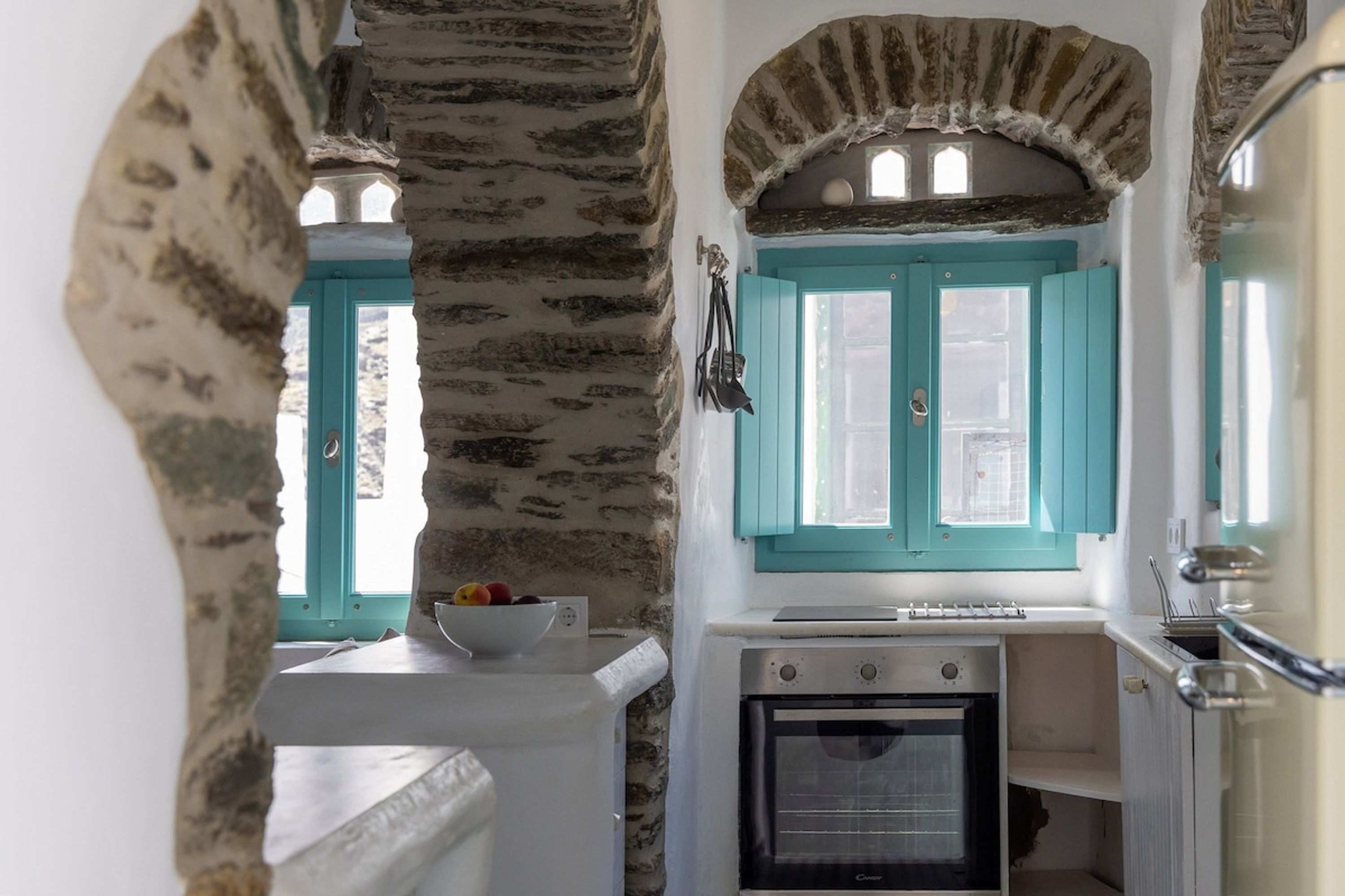 A compact kitchen with a stone wall, a teal-framed window, and a small oven.
