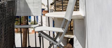 Un balcon avec une chaise blanche, une table et un petit tabouret en bois.