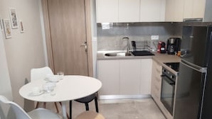 Angolo cottura compatto con zona pranzo, comprensivo di tavolo, sedie e frigorifero.