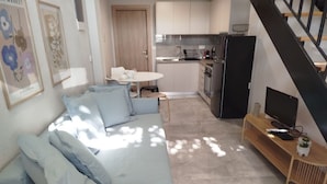 Un soggiorno con un divano, una TV su un supporto in legno e una cucina sullo sfondo.