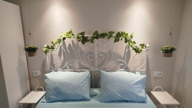 Una camera da letto con un letto, due comodini, una testiera decorativa in metallo e piante pensili.