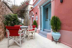 Un espace extérieur accueillant avec des chaises rouges et une table, une porte bleue et des plantes en pot.