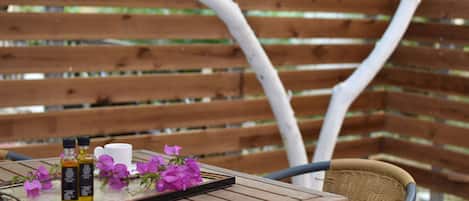A wooden table with a tray holding two bottles, a cup, and purple flowers.