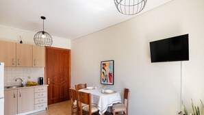 A modern kitchen with wooden cabinets, a dining table with chairs, a TV mounted on the wall, and a potted plant. - Casa Vardani 3 Modern Central Apartment (Lefkada)