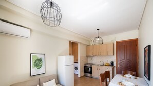 A compact living space with a sofa, dining table, kitchen area, and a ceiling light fixture. - Casa Vardani 3 Modern Central Apartment (Lefkada)