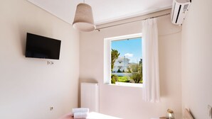 A bedroom with a bed, a TV, an air conditioner, a window with a view, and a radiator. - Casa Vardani 3 Modern Central Apartment (Lefkada)