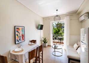 A dining area with a table set for two, a potted plant, a TV mounted on the wall, and a balcony with outdoor furniture. - Casa Vardani 3 Modern Central Apartment (Lefkada)