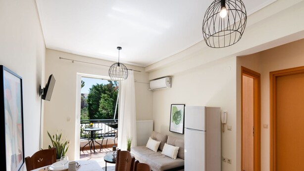 A compact living space with a dining area, a sofa, a refrigerator, and a balcony with a table and chairs. - Casa Vardani 3 Modern Central Apartment (Lefkada)