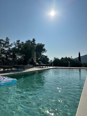 Une piscine aux eaux cristallines, bordée de chaises longues et agrémentée d’un flotteur, le tout entouré d’arbres et avec une montagne en toile de fond.