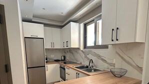 Una cocina moderna con armarios blancos, un refrigerador de acero inoxidable, una isla de madera con taburetes altos y un salpicadero de mármol.