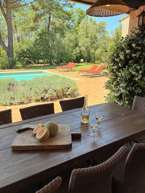 A wooden table with a bottle of white wine, two glasses, and a half-cut melon. - 4-bedroom villa with a private padel court, pool, and petanque court   (Le Muy)