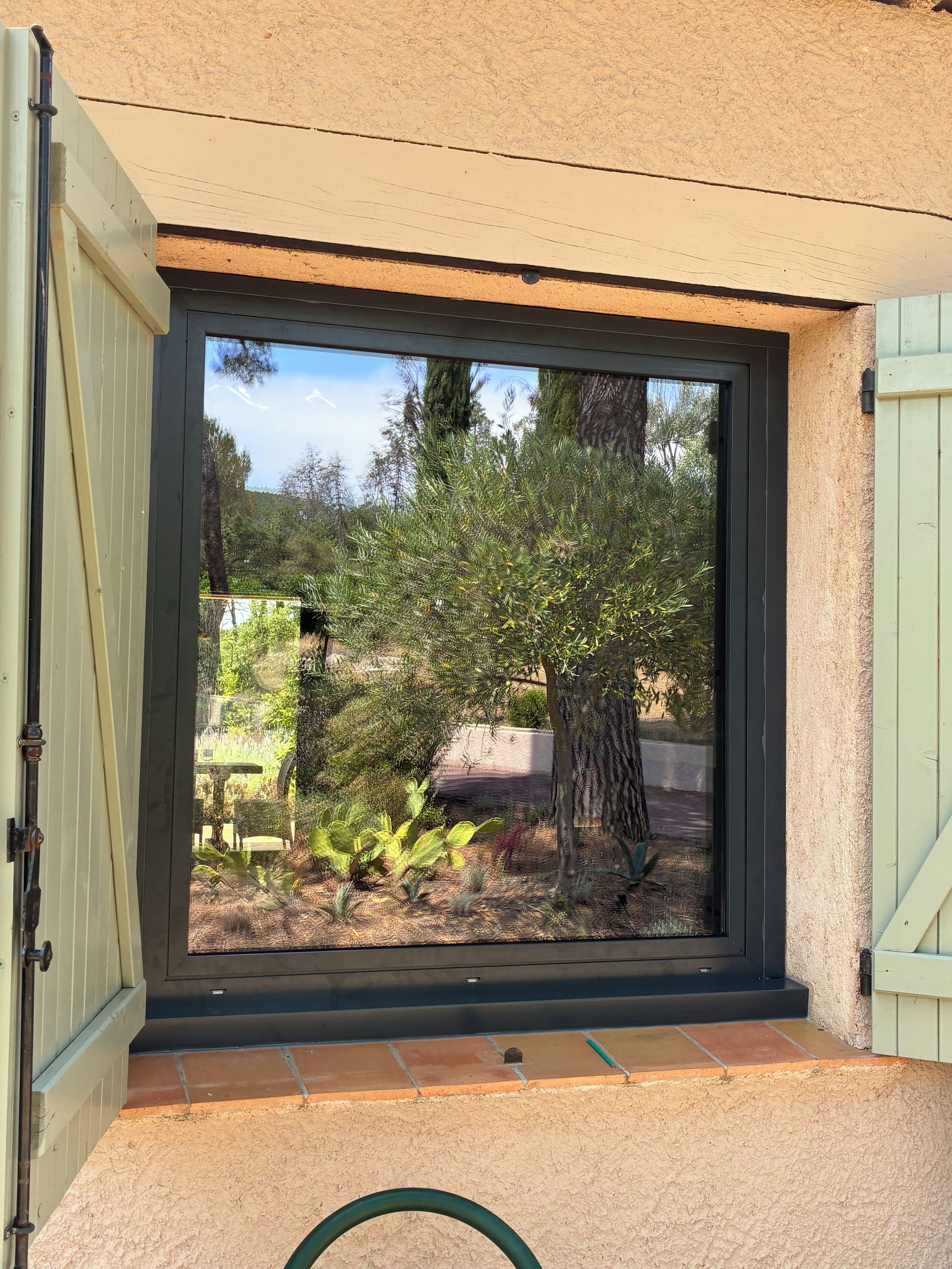 Ein Fenster mit Blick auf einen Garten, einen Baum und eine Terrasse.